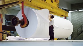 Men checking quality of finished industrial paper roll.