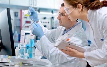 Man and woman in lab coats looking at a test tube containing green liquid.